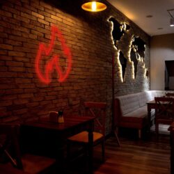 A dimly lit cafe with brick walls, wooden tables and chairs, a backlit world map wall decoration, and a red Neon Fire sign.