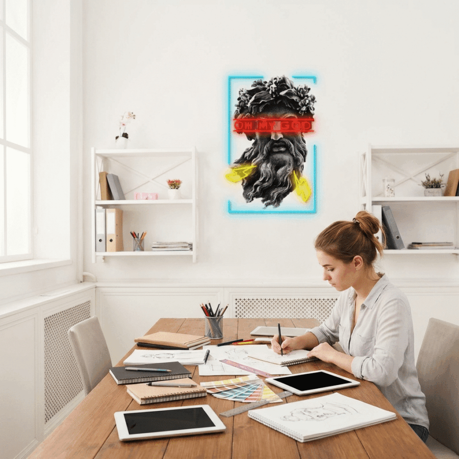 A woman works at a desk with a tablet and color samples in a modern office; behind her is the "Oh My God Neon Sign" featuring a bearded face with "OH MY GOD" over the eyes.