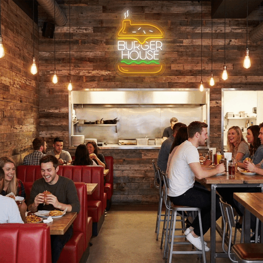 Guests enjoy dining and socializing in Neon Burger House, a casual spot with red booths, wooden walls, and a glowing neon "Burger House" sign above the open kitchen—perfect for #BurgerLove.