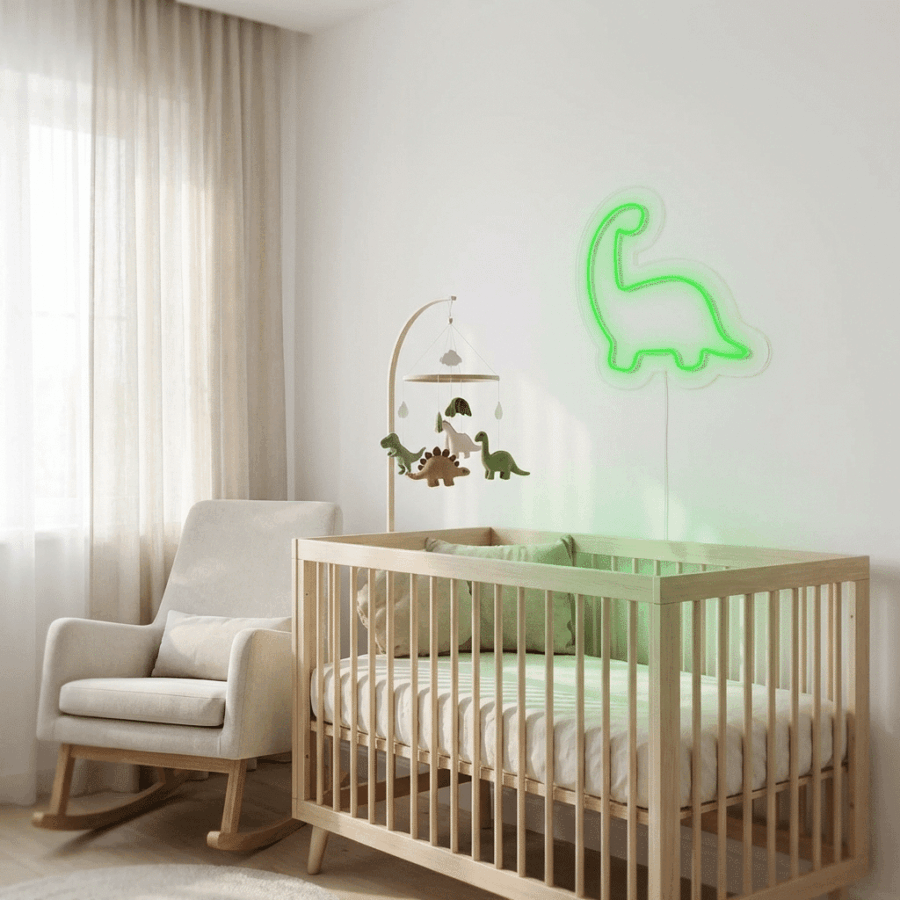 A nursery with a wooden crib, dinosaur mobile, beige rocking chair, and the Dino Neon green dinosaur-shaped light on the wall. Light curtains drape the window, gently illuminating the softly lit room.