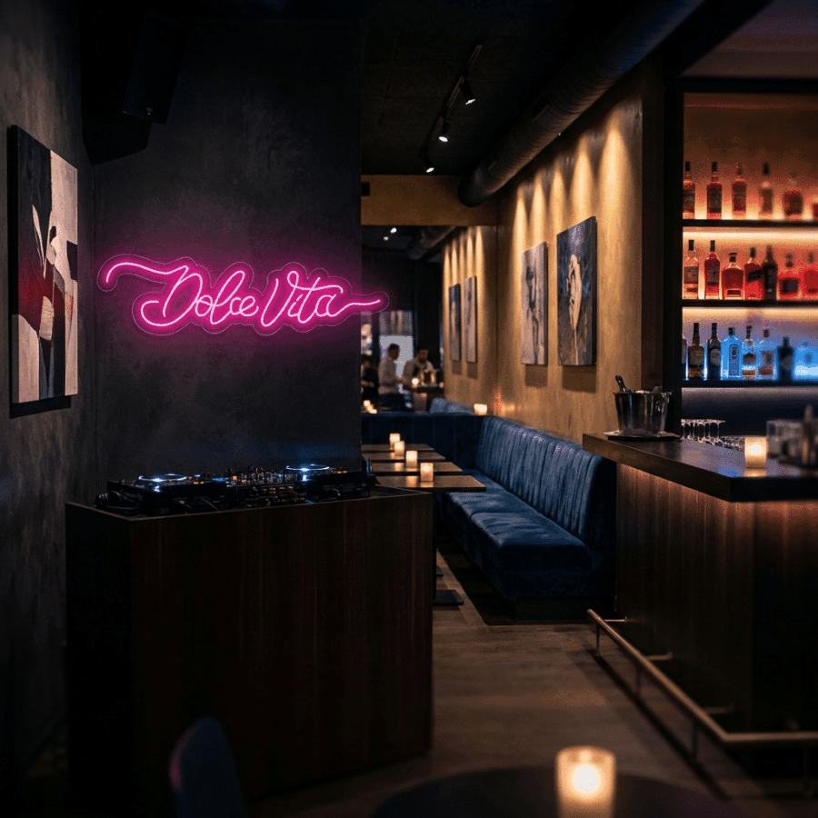 A dimly lit bar features a Neon Dolce Vita sign, blue velvet seats, candlelit tables, a DJ booth, and shelves of liquor bottles lining the wall.