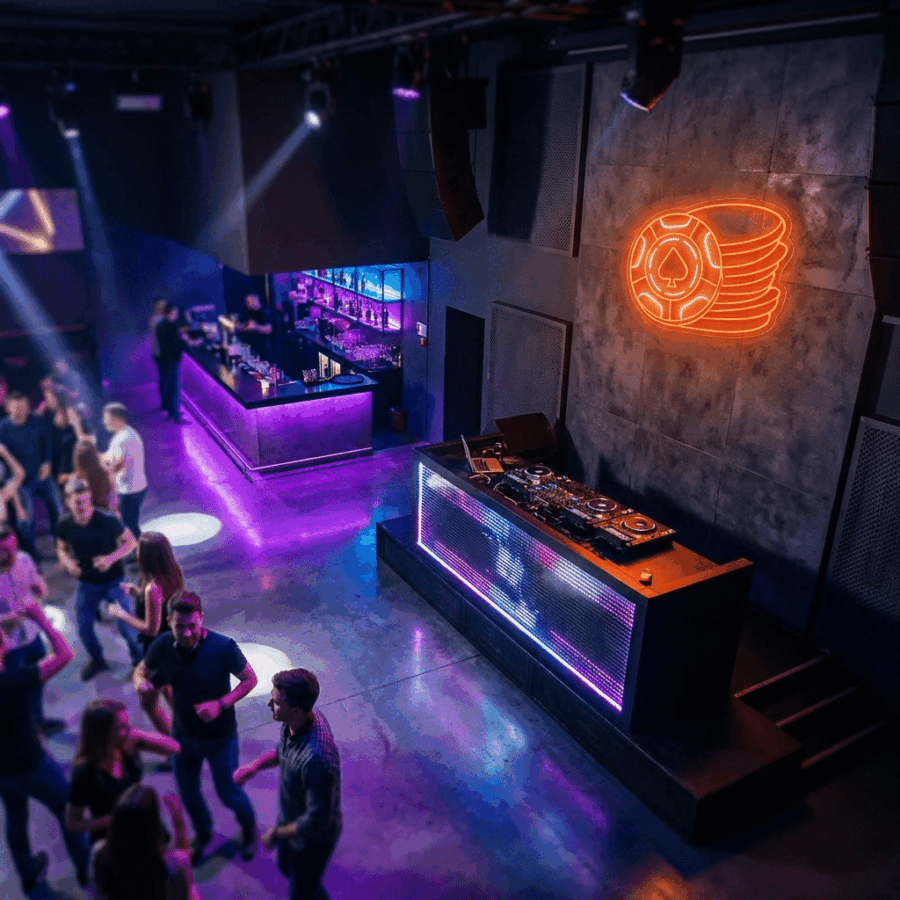 Modern nightclub interior featuring a Poker Chip Neon sign, DJ booth, purple lighting, people dancing, and a bar in the background.