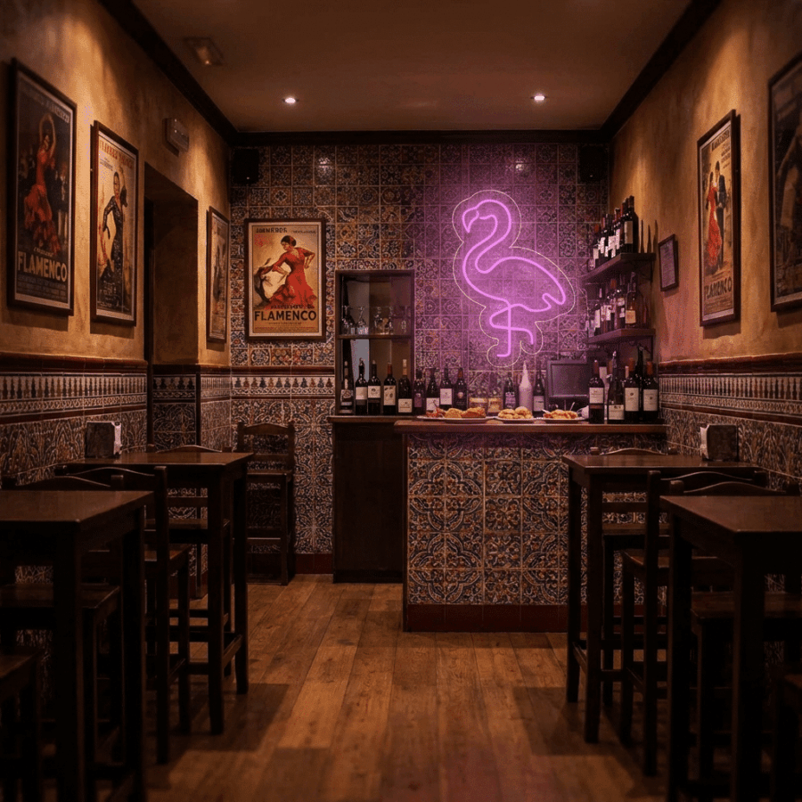 A small, dimly lit bar with tiled walls, wooden tables, flamenco posters, and the vibrant Flamingo Neon sign glowing above a wine display behind the counter.