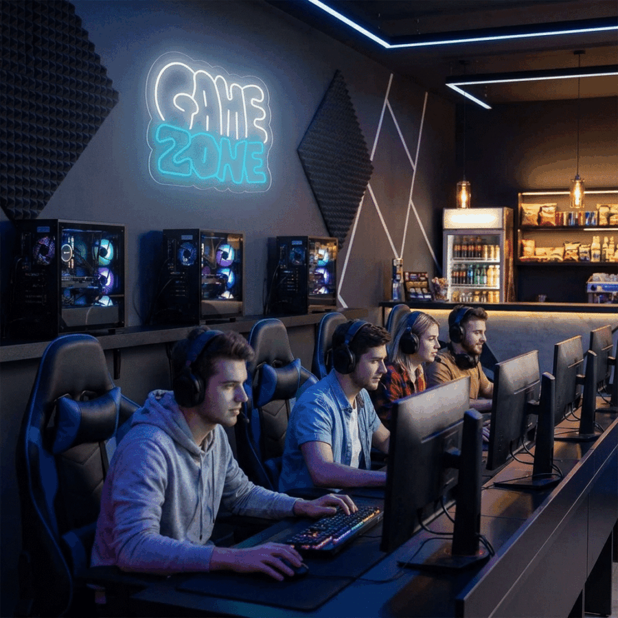 Four people sit at computers in a gaming lounge, illuminated by the Neón Game Zone Dos Colores sign, with gaming PCs and snacks in the background.