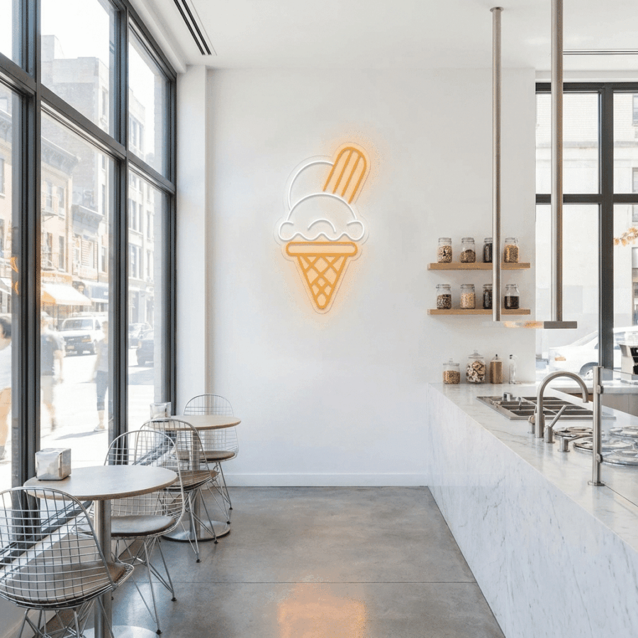 A minimalist ice cream shop features metal chairs, small round tables, a marble counter, jars on shelves, and an Ice Cream Cone Neon glowing on the wall as large windows bathe the space in natural light.