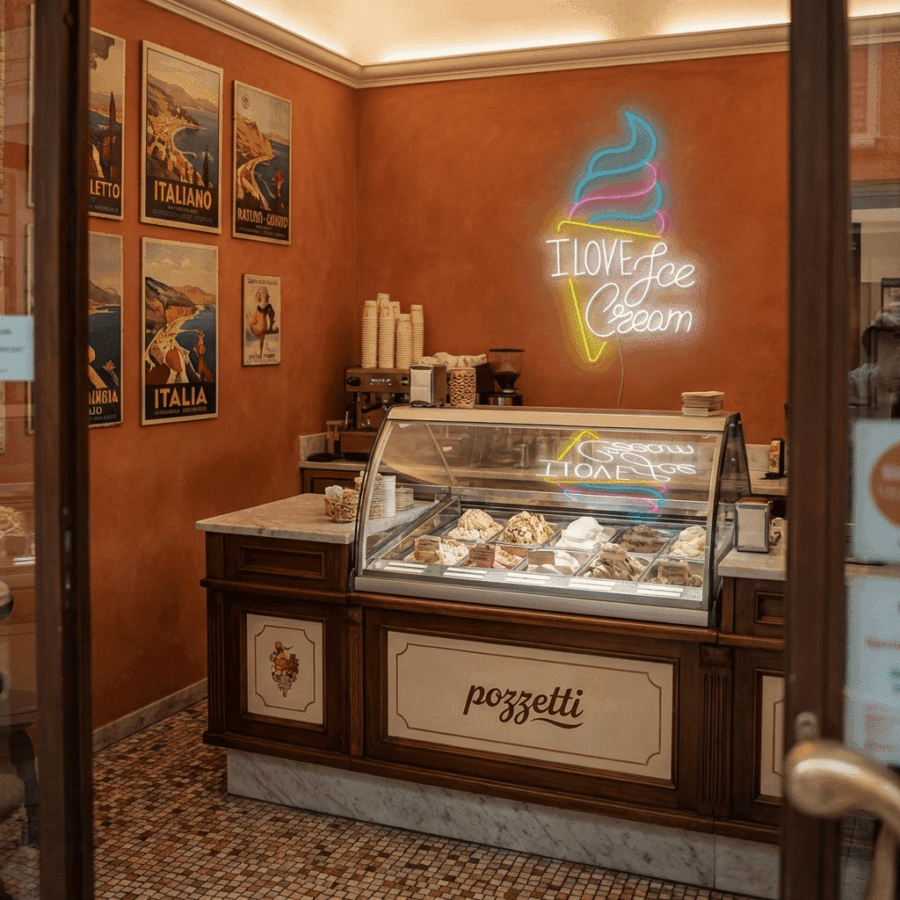 A small gelato shop interior features a display case of assorted gelato, vintage Italian posters, and the Neon I Love Ice Cream sign glowing on the wall.