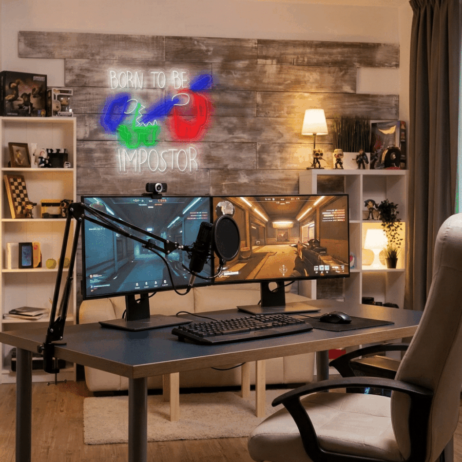 A modern gaming setup with dual monitors, keyboard, microphone, and gaming chair. The Neon Neon Among Us sign glows on the wall above shelves filled with books, decor, and figurines.