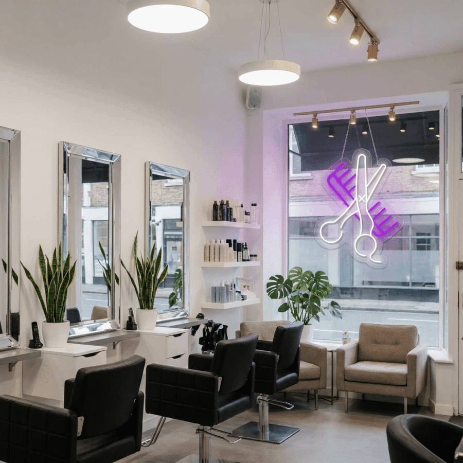Modern hair salon interior with black chairs, white counters, large mirrors, potted plants, and a stylish Neon Comb and Scissors sign illuminating the window.