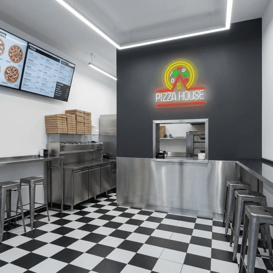 Modern pizza restaurant interior featuring a black-and-white checkered floor, metal counter, bar stools, stacked pizza boxes, digital menu, and the Neon Pizza House sign glowing brightly on the wall.