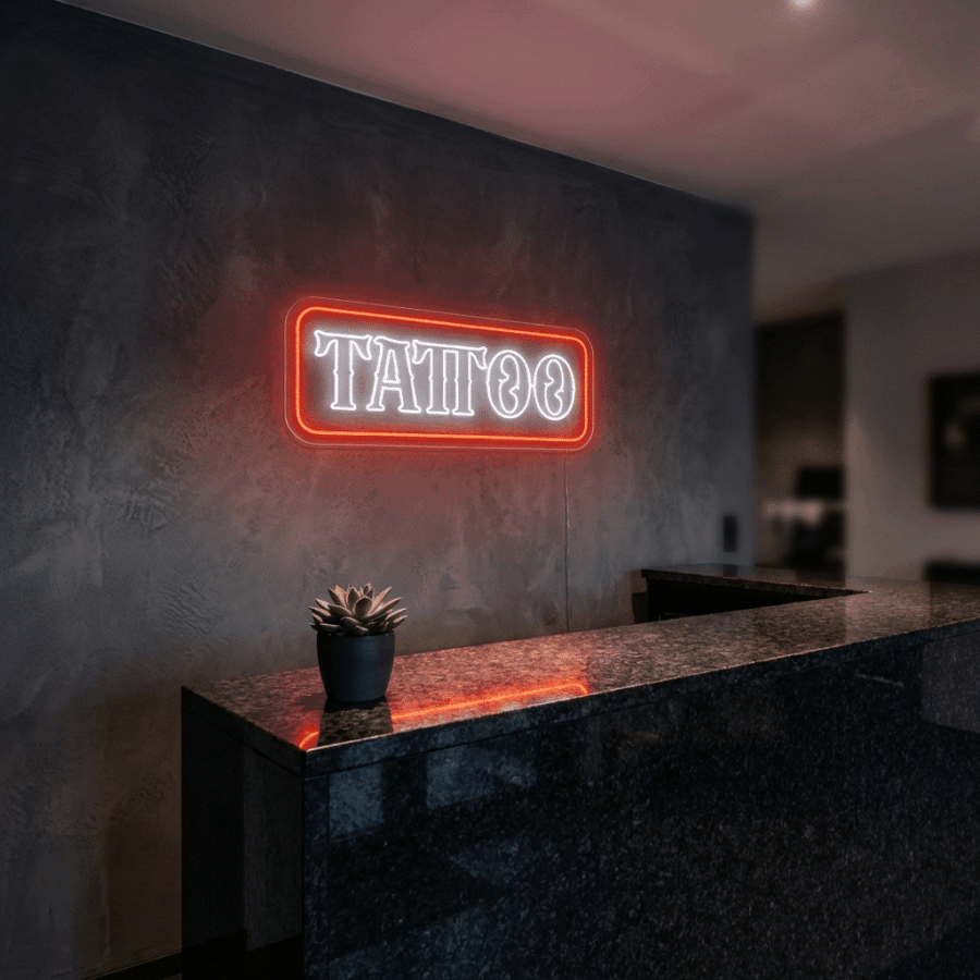 The Neon Tattoo sign, glowing red, is displayed on a dark gray wall above a black marble counter with a small potted plant.