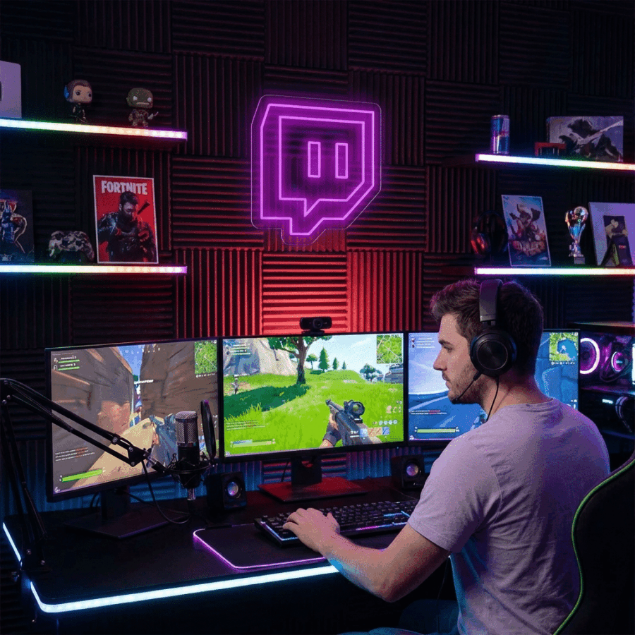 A man wearing headphones streams a video game at a dual-monitor setup with neon lights, including the Twitch Neon sign, and gaming merchandise on shelves in the background.