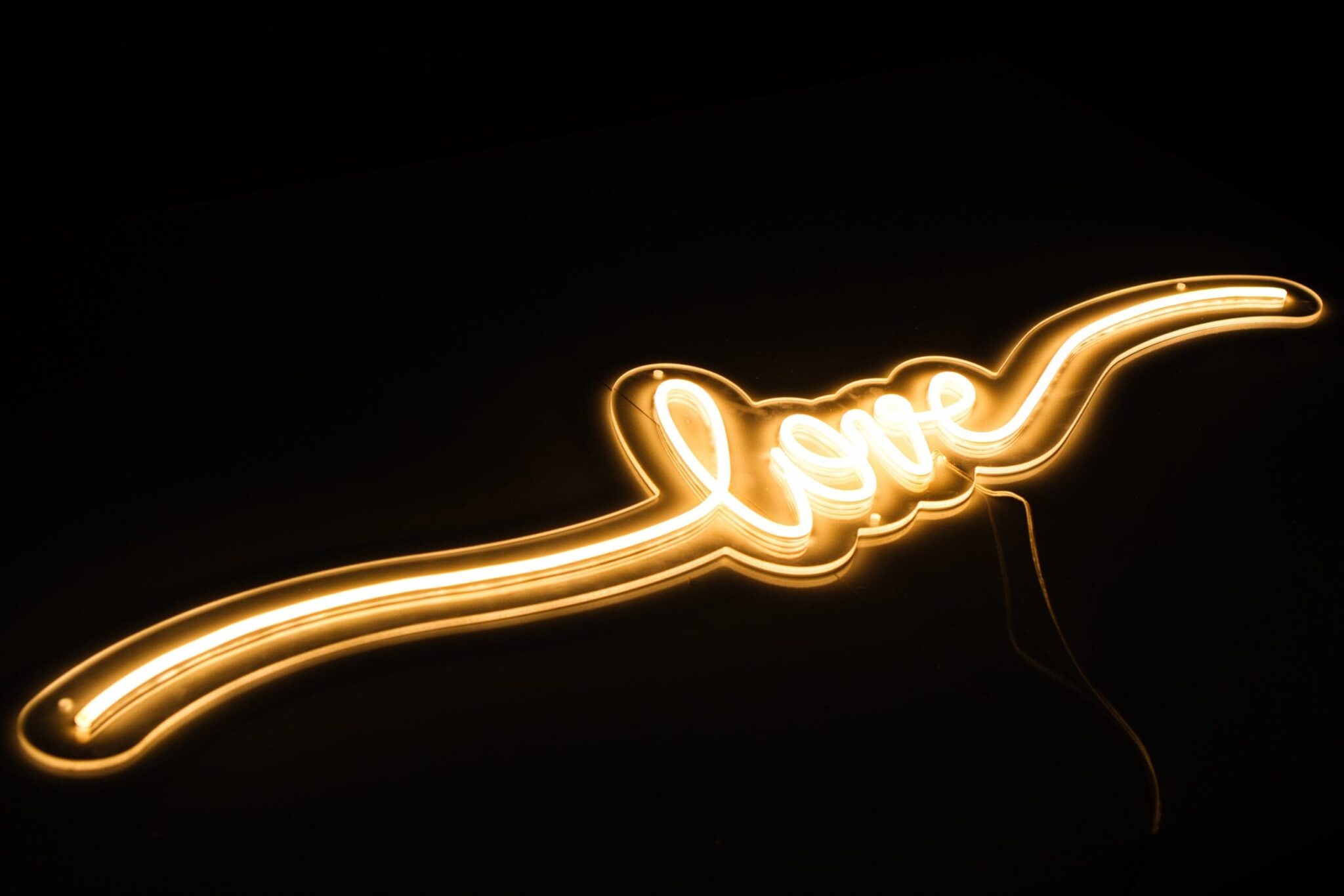 Neon Love is a glowing neon sign that spells out "love" in flowing cursive, with extended lines framing both sides, creating a bright and romantic display in the dark.